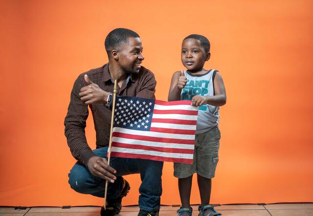 A father and a son holding a United States flag together. 