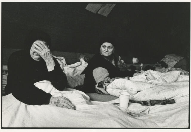 Two Bosnian women lie in beds in a refugee camp in Croatia, one of whom is crying.