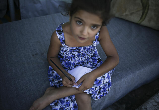 7-year-old writes in her notebook outside a tent