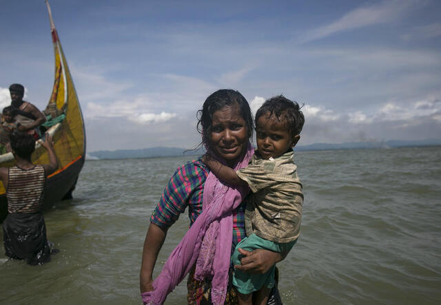 A Rohingya woman carries her child to shore in Bangladesh after fleeing violence in Myanmar's Rakhine State by boat. 