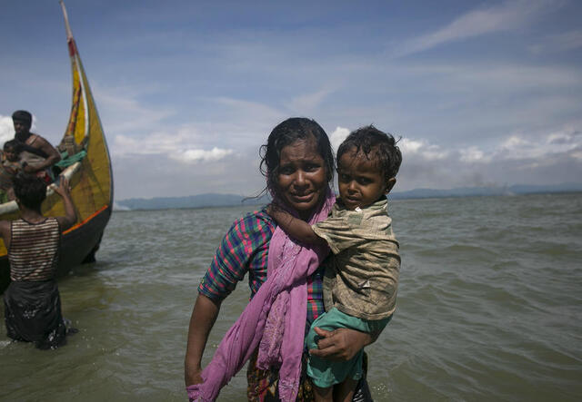 A Rohingya woman carries her child to shore in Bangladesh after fleeing violence in Myanmar's Rakhine State by boat.
