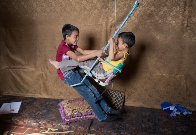 Two Syrian boys play on a homemade swing in their tent