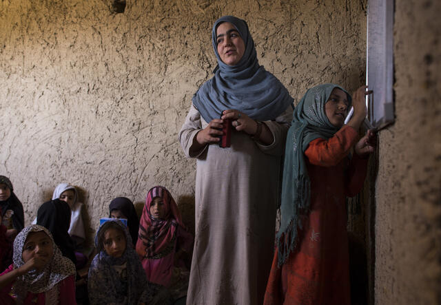 A teacher leads her class in Afghanistan as a girl writes on the board