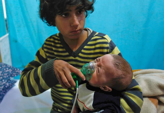 A Syrian boy holds an oxygen mask over the face of an infant at a make-shift hospital 