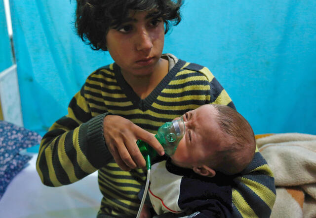 A Syrian boy holds an oxygen mask over the face of an infant at a make-shift hospital