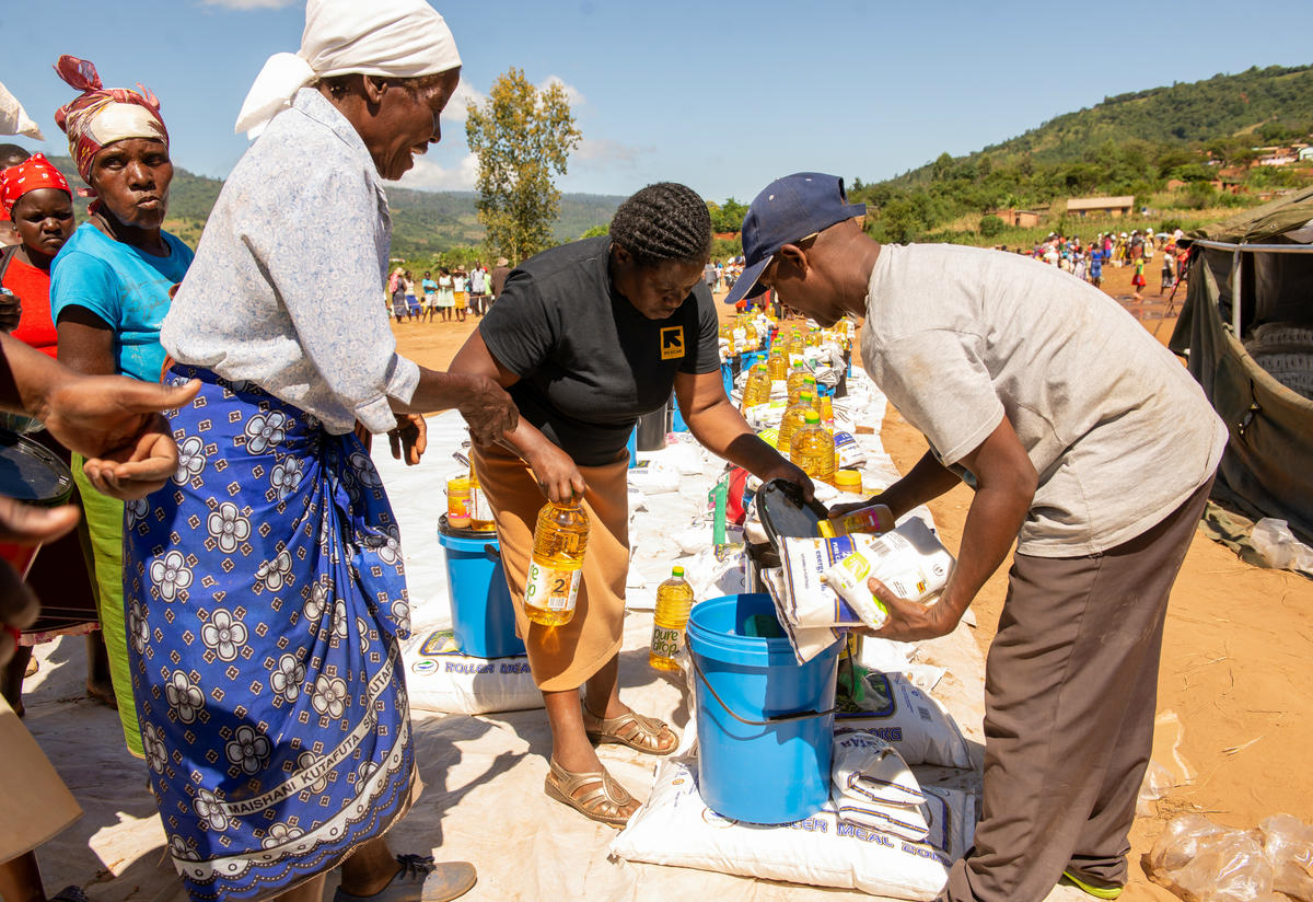 tow IRC aid workers help a woman pack a bottle of cooking oil and other food aid and emergency supplies in Machongwe, Zimbabwe