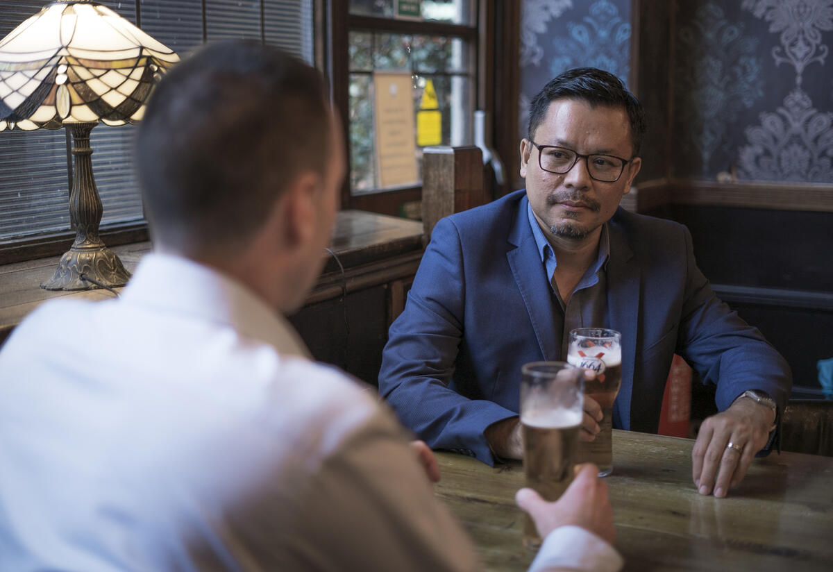 Darren and Warren talk at a pub table over over pints of beer