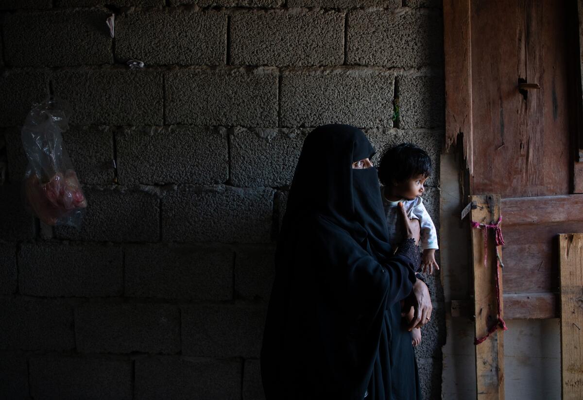 Adeeyah Aholds her toddler daughter Salaman in the dark kitchen of their temporary home in Yemen. The family received assistance from the International Rescue Committee.
