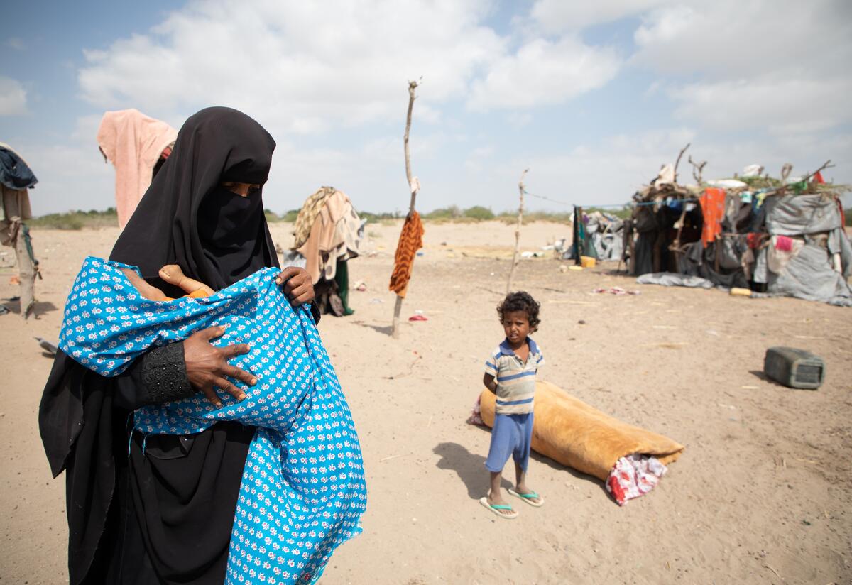Nadia holds her baby son wrapped in a blanket outside her makeshift home in Yemen. The family received medical and nutrition assistance from the International Rescue Committee.