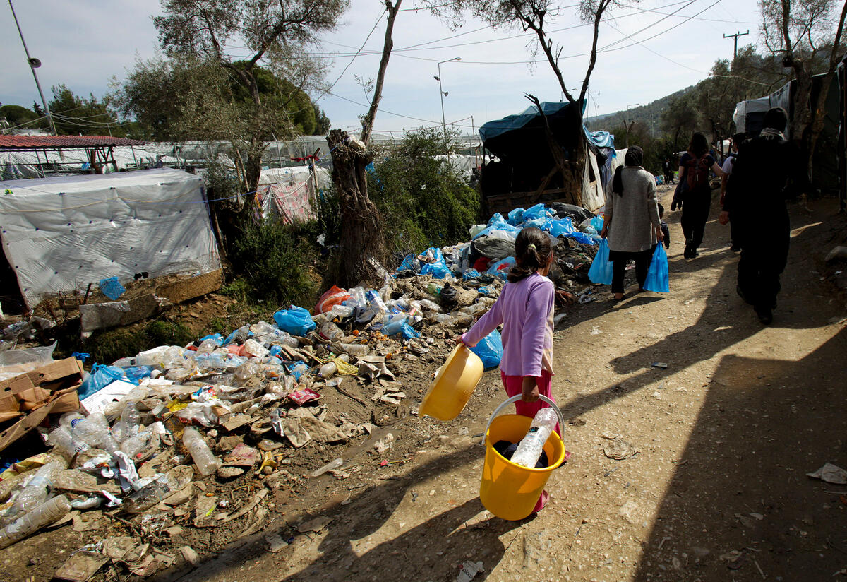 A young girl walks past tents and trash in an overcrowded refugee center