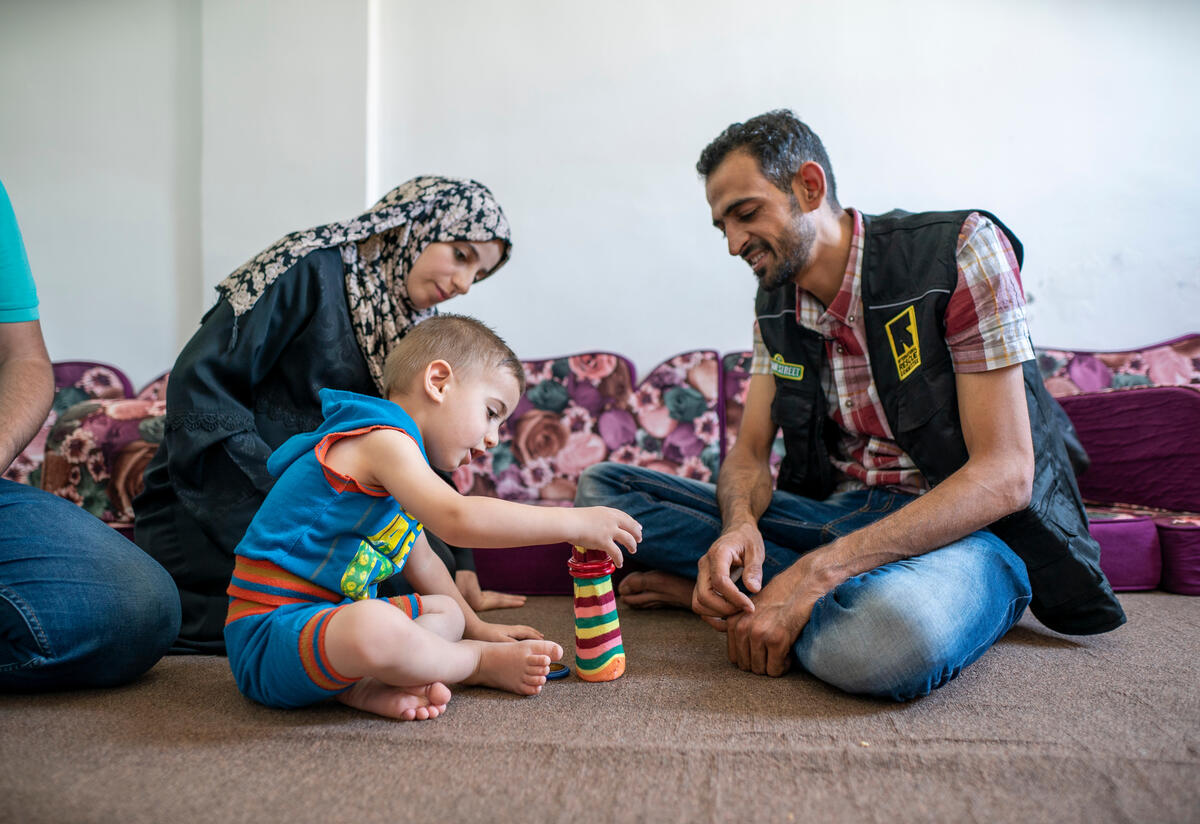 International Rescue Committee volunteer Anas demonstrates playful learning techniques to thr parents of 2-year-old Rashid. Anas, an IRC Reach Up & Learn volunteer and Syrian refugee plays stacking rings with 2-year-old Rashid at his family's home.