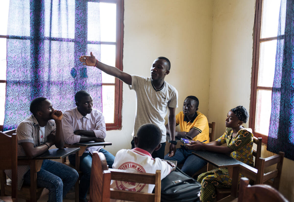 Youth leader Benjamin stands inside a circle of seated teenagers, pointing as he gives an IRC-supported training on Ebola.
