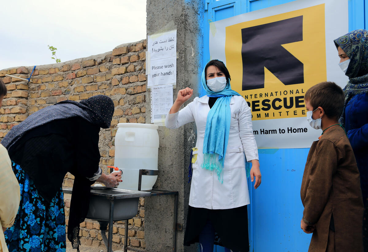 IRC hygiene promotor Sohalia Khaliqi provides training and critical information about COVID-19 to women, men and children in Herat province, Afghanistan An IRC health educator wearing a face mask gestures as she talks to a group of people gathered outdoors in Afghanistan about the COVID-19 crisis.