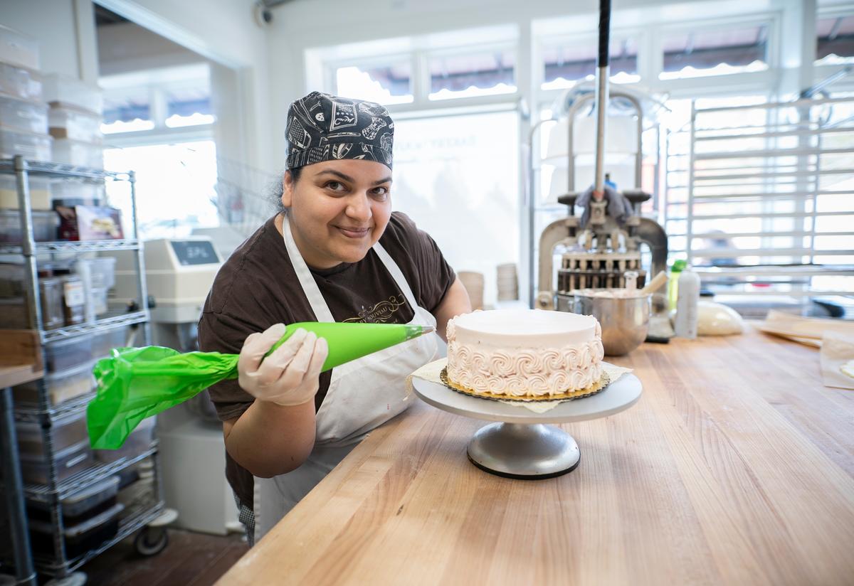 Taghreed, wearing a baker's apron, pipes decorative icing onto a cake at a bakery in Seattle.