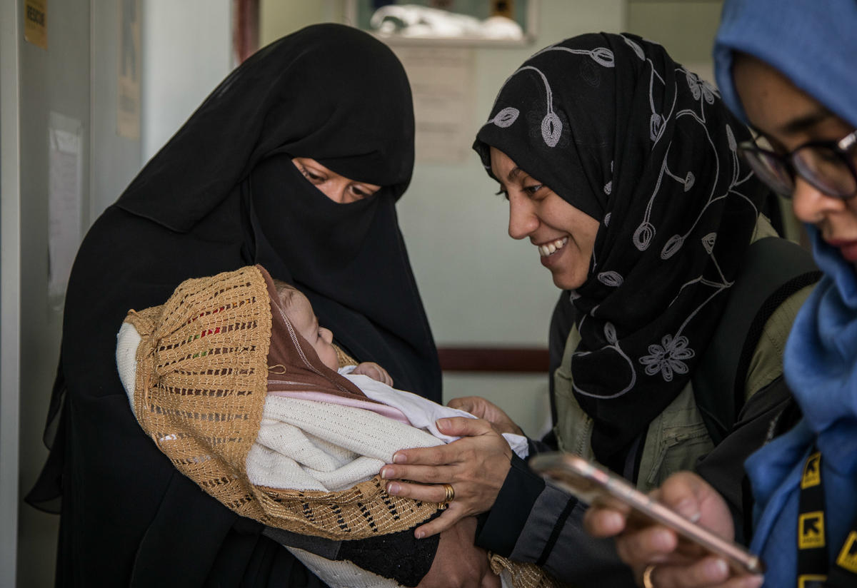 IRC nutrition manager Sara plays with Mona's baby, held in her mother's arms. 