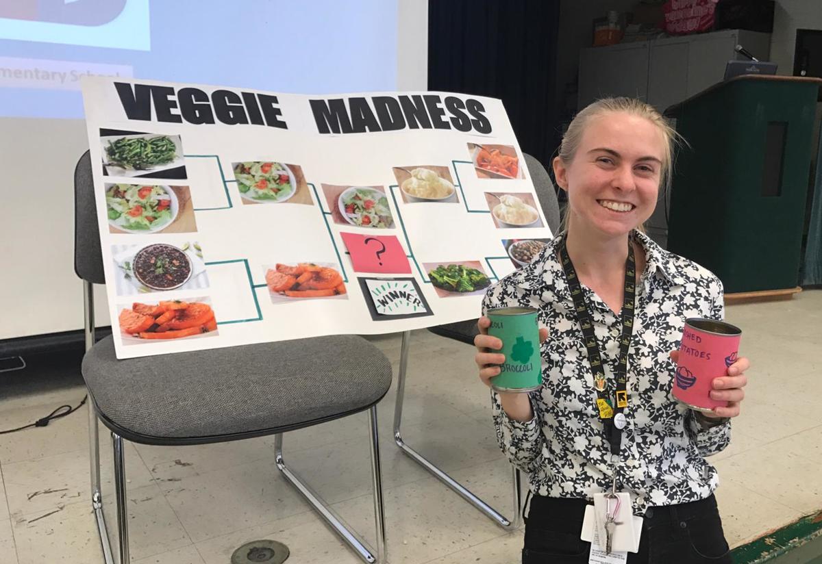 FoodCorps Member Meggie stands beside her vegetable bracket poster and holds two containers for children to cast their votes.