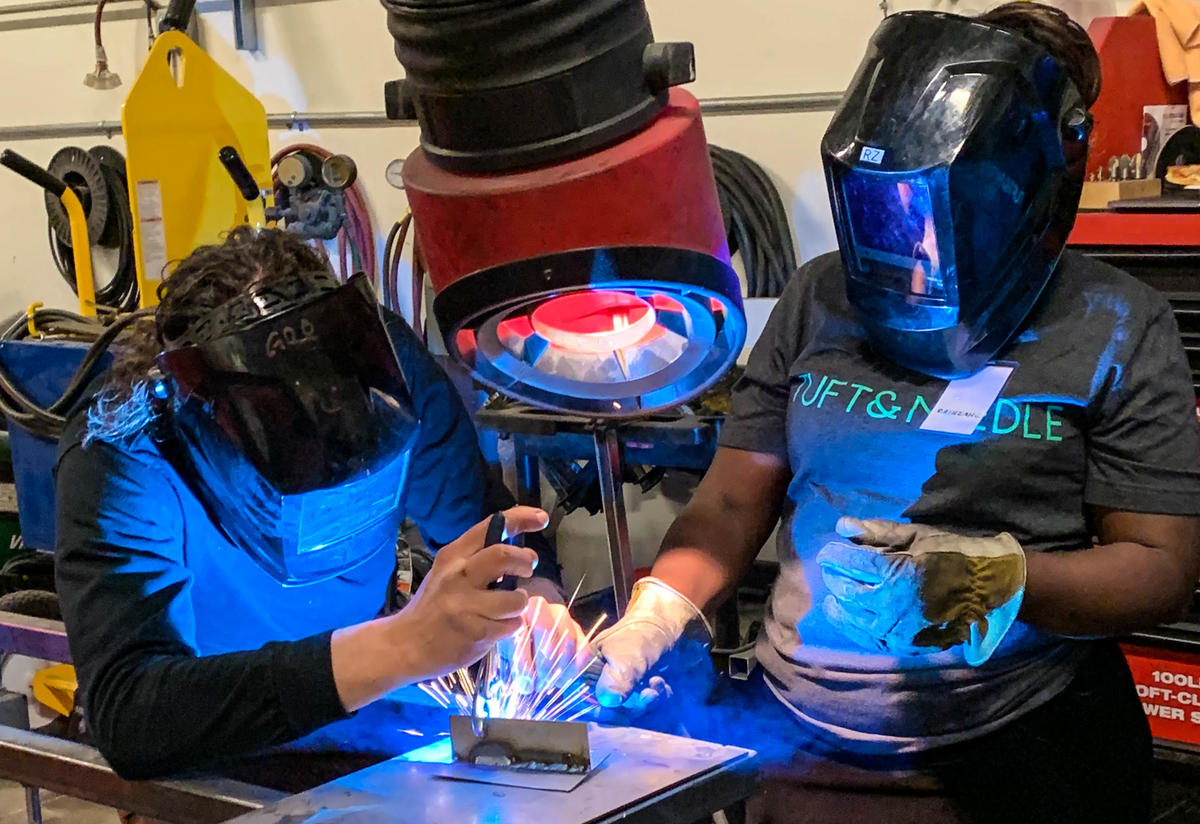 Two people wearing protective face shields are welding in a factory to gain experience with tools.