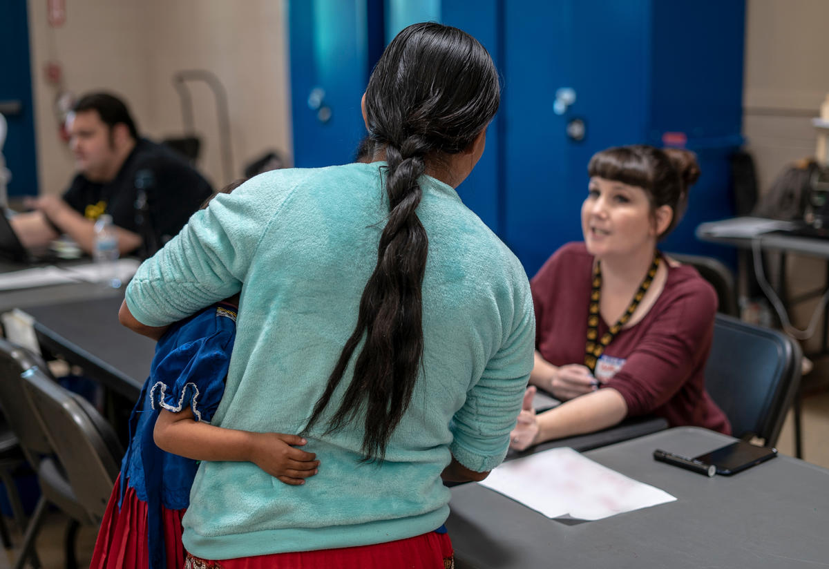 The back of a woman with her arms around her son speak with an IRC employee while checking in at the Welcome Center