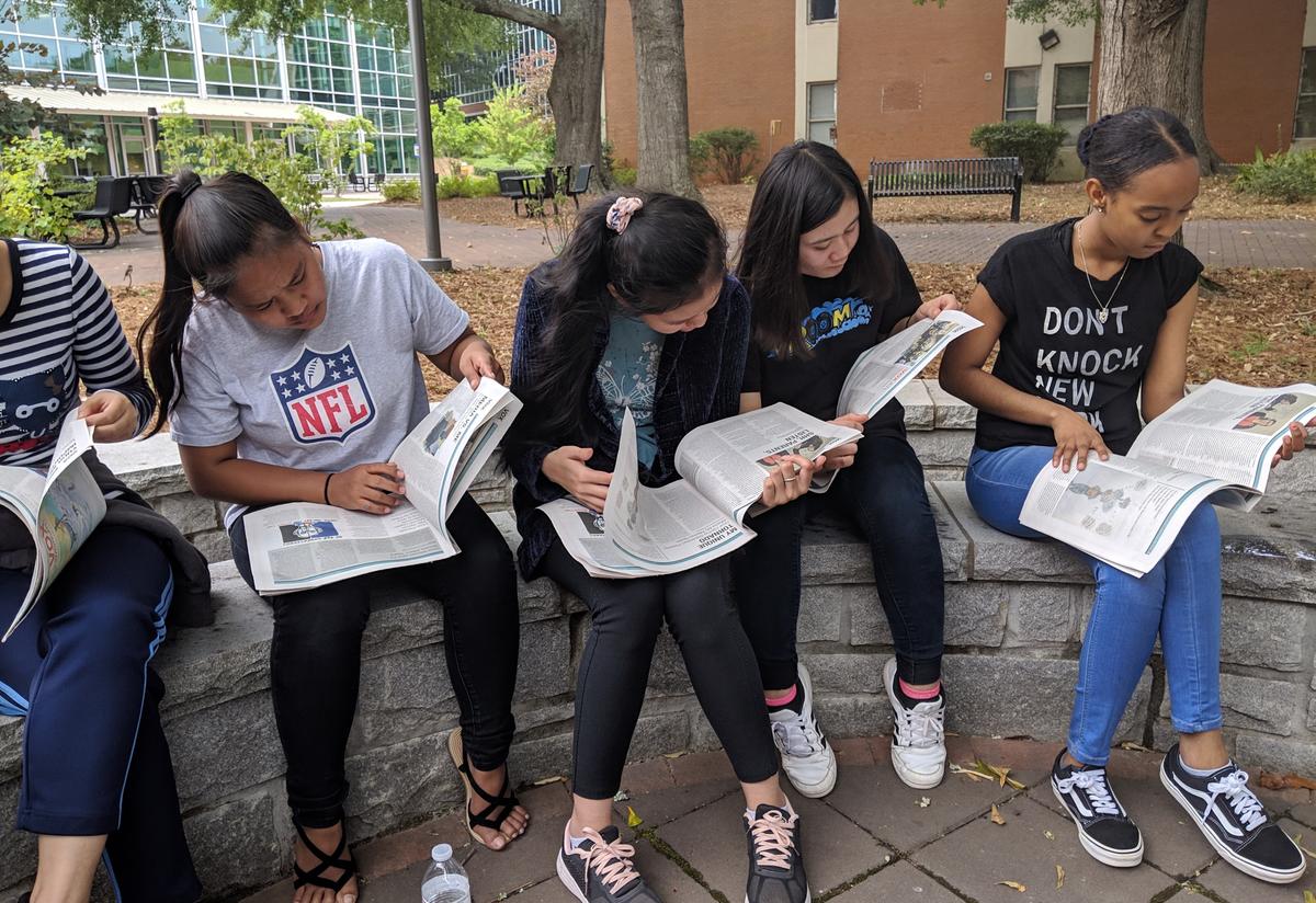 Students enjoyed a taste of campus life! Four students are reading teen newspapers outside on a college campus.