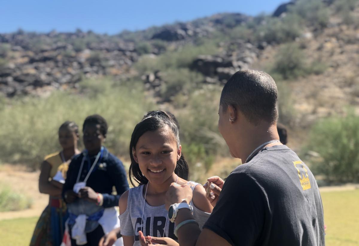 In the forefront, a refugee girl laughs with an IRC staff member. In the background three girls stand.