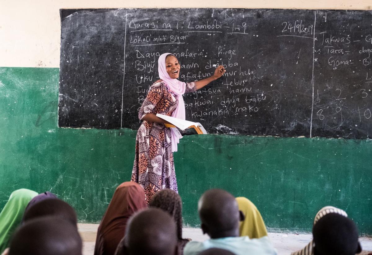 An International Rescue Committee teacher leads her class in Nigeria. An IRC teacher at the blackboard in Nigeria. She teaches her students academic subejcts and techniques to help them cope with life in a conflict zone.