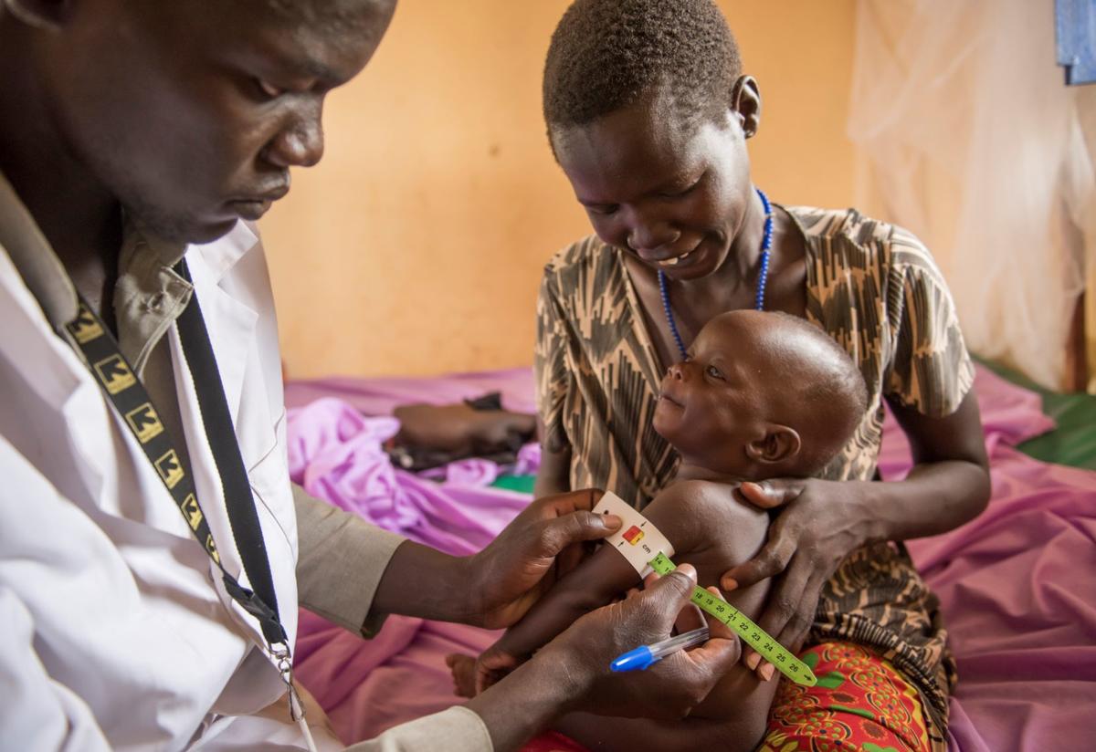 An IRC health worker examines a 7-month-old infant being held by his mother.