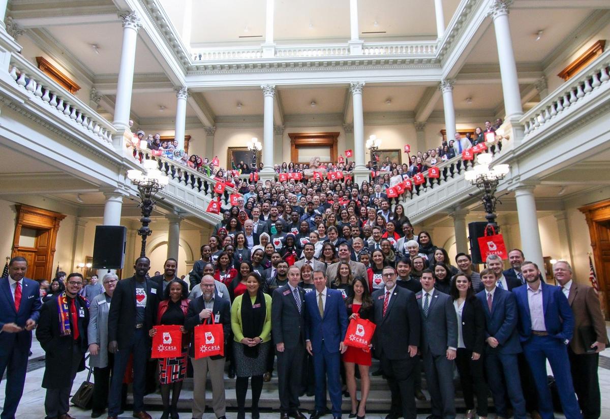 New Americans Celebration attendees take a picture with Governor Brian Kemp in February 2019. More than 300 volunteer advocates and new Americans stand on and around a large marble staircase at the Georgia State Capitol to take a group picture with Governor Brian Kemp and members of the GA General Assembly.