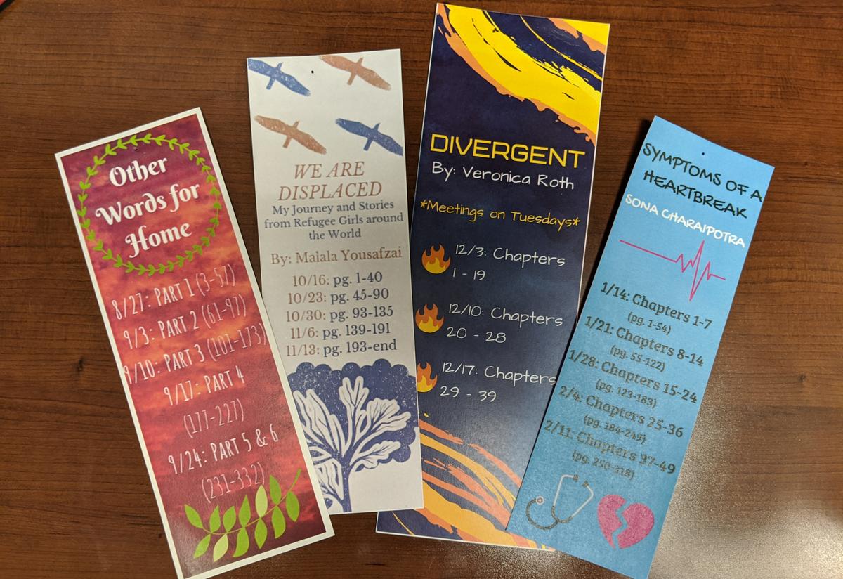 Our Youth Futures Book Club is already on book number four of the school year! Four colorful bookmarks are arranged on a desk. Each bookmark has the name and author of a different book, as well as a reading schedule for the students to follow.
