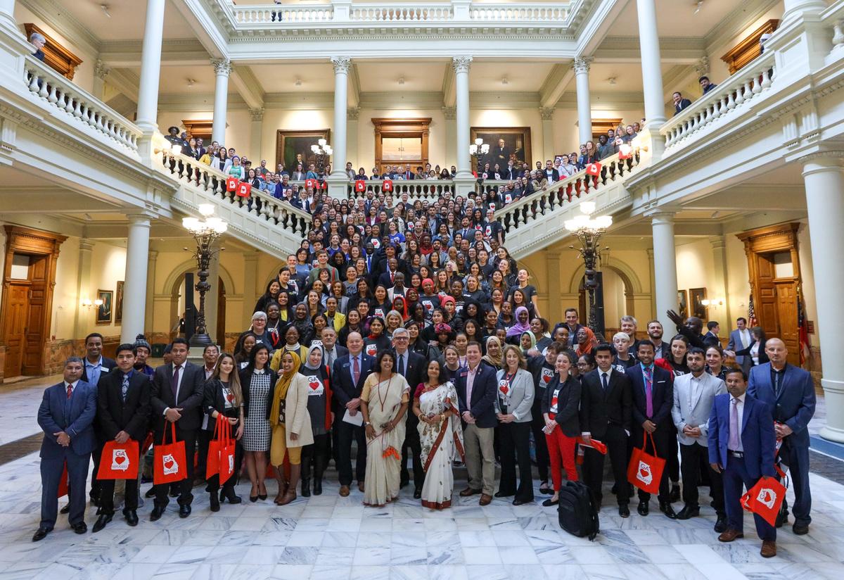 More than 300 people representing many different countries and ethnicities pose for a group photo on a huge marble staircase in the middle of the Georgia State Capitol building. Members of the legislature stand in the front row.