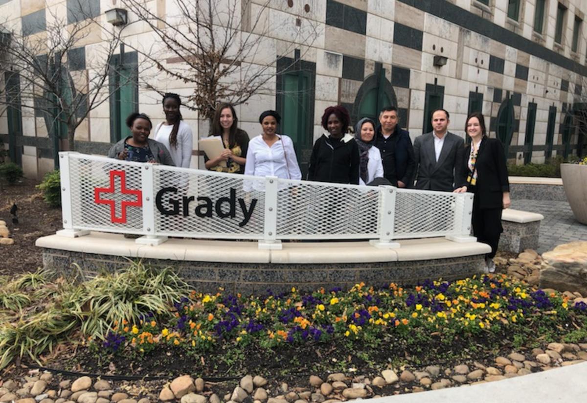 Six IRC clients and two staff members stand proudly together behind a Grady Hospital sign.