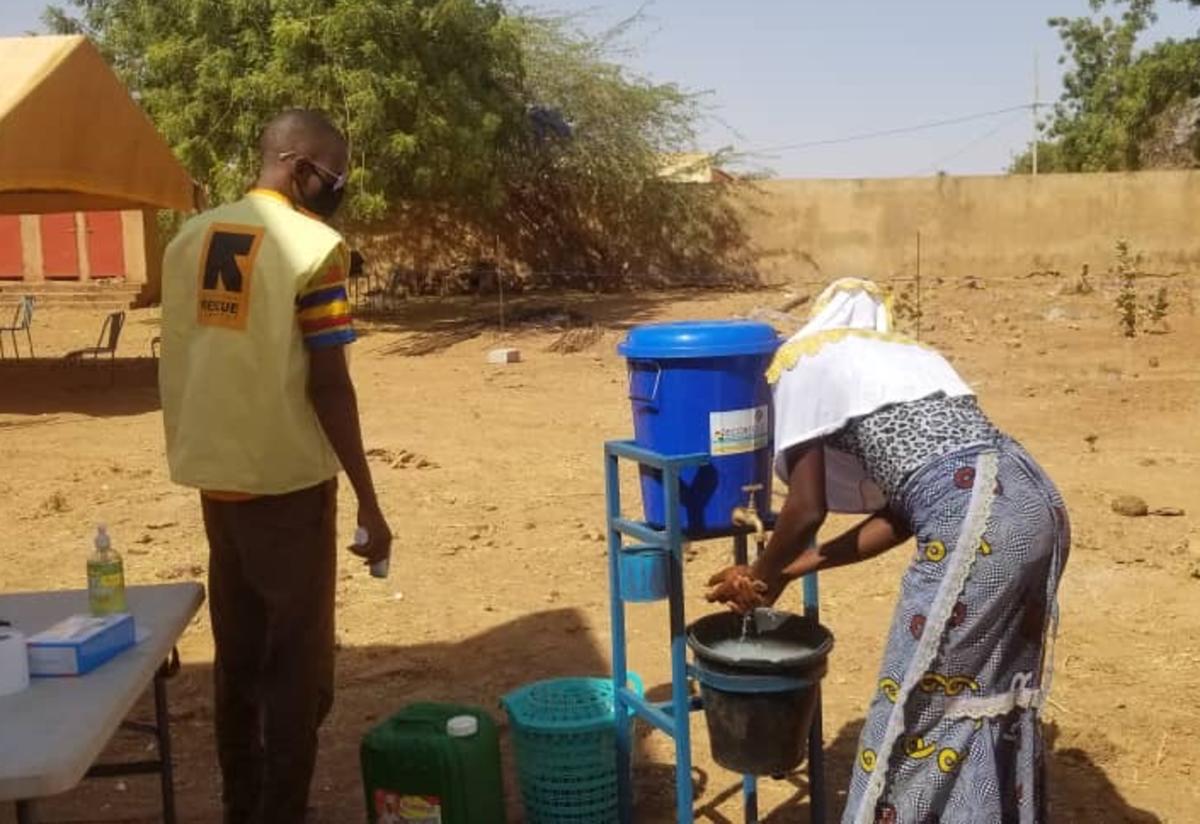 Staff distribute soap and hold community trainings in Burkina Faso. A woman washes her hands while an IRC staff member looks on in Burkina Faso