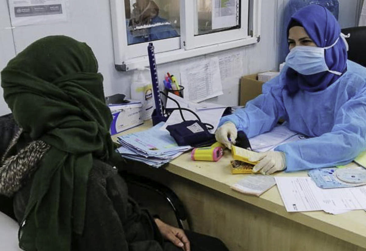 An IRC midwife wearing Personal Protective Equipment, or PPE, sits at a desk and talks with an IRC client.