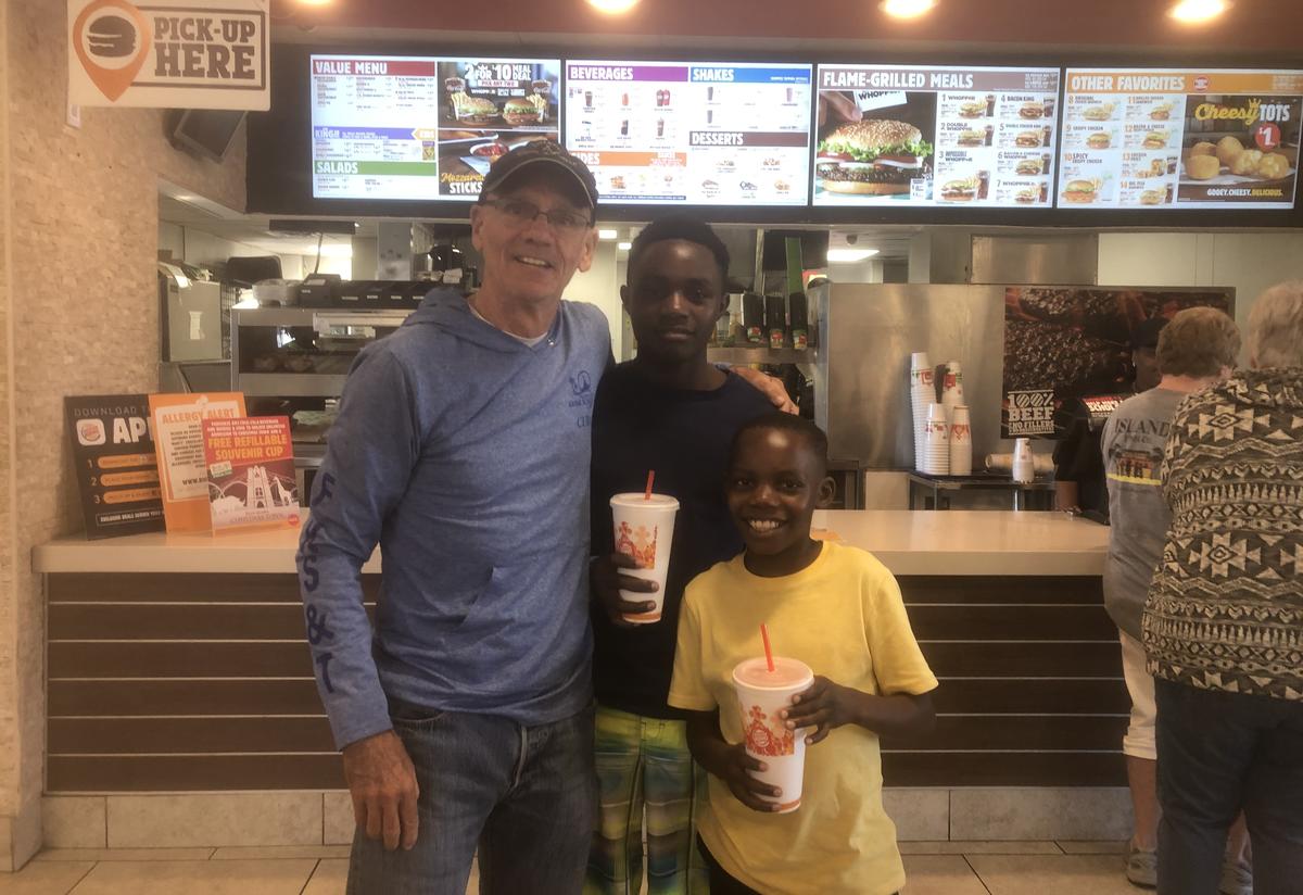 Tommy took mentees Eric and Emmanuel for their first Burger King experience. Tommy stand with his arm around Eric and Emmanuel in front of the Burger King counter. The boys hold large sodas and are smiling.