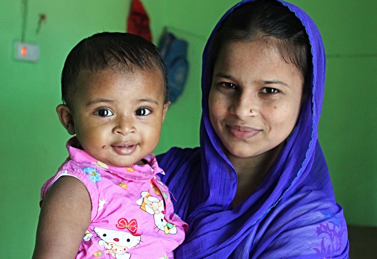 Lovely Akter, an IRC midwife, poses with her nine-month-old daughter Lovely Akter, an IRC midwife, poses with her nine-month-old daughter. Lovely is wearing a blue headscarf and her daughter is wearing a pink shirt. Both are smiling.