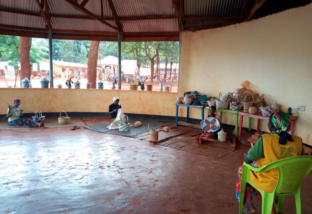 Women in one of the IRCs safe spaces for women in Tanzania practice basket weaving while maintaining social distancing. In an IRC-run safe space for women in Tanzania three woman sit on the ground six feet apart while practicing basket weazing. An IRC staff member sits on a chair facing them.