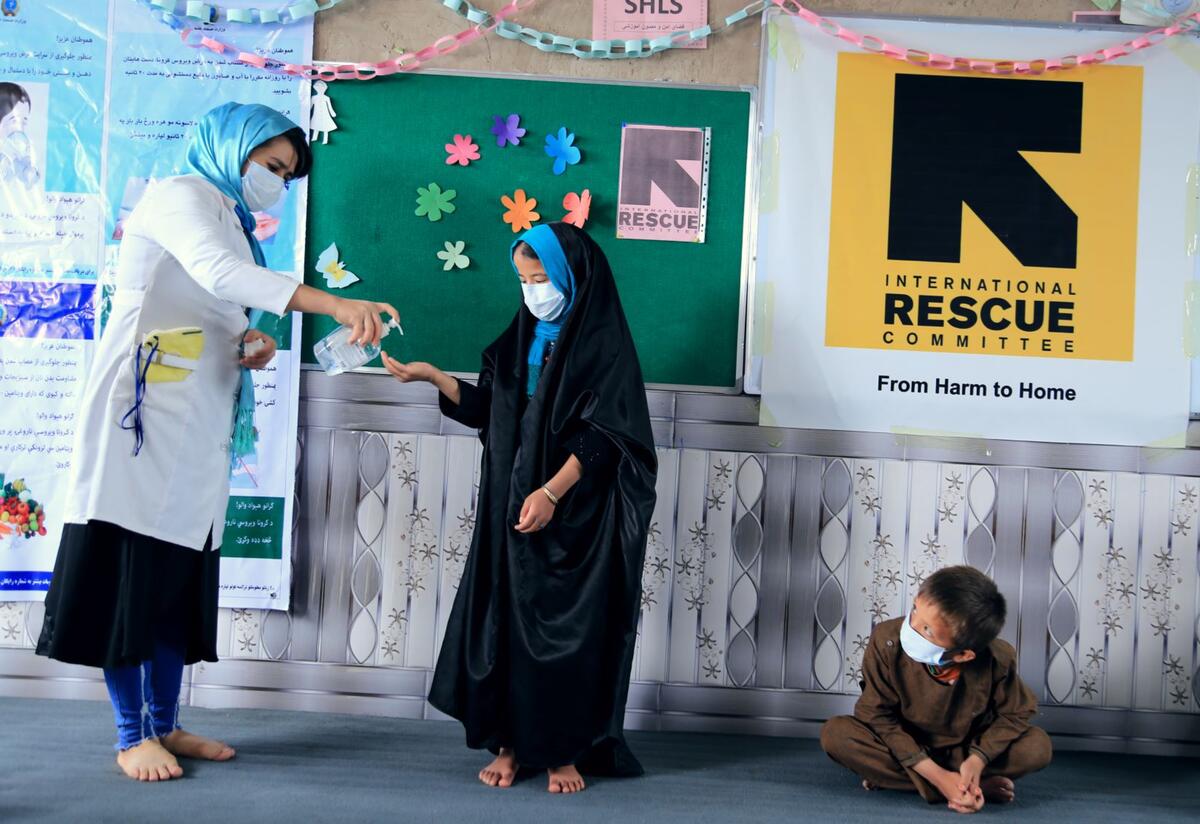 IRC hygiene promoter Sohalia Khaliqi provides training and critical information about COVID-19 to children in Herat province, Afghanistan. IRC hygiene promoter Sohalia Khaliqi, wearing a mask, squirts hand soap onto the hand of a child, also wearing a mask, while another child looks on. She is providing training and critical information about COVID-19 in Herat province, Afghanist
