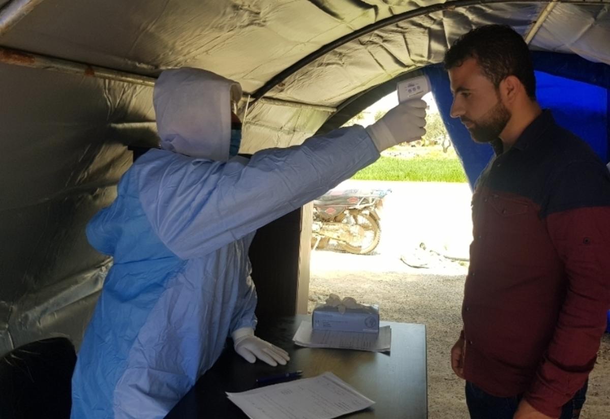 A health worker takes a patient’s temperature before they enter a clinic run by the IRC in a town in northwest Syria.