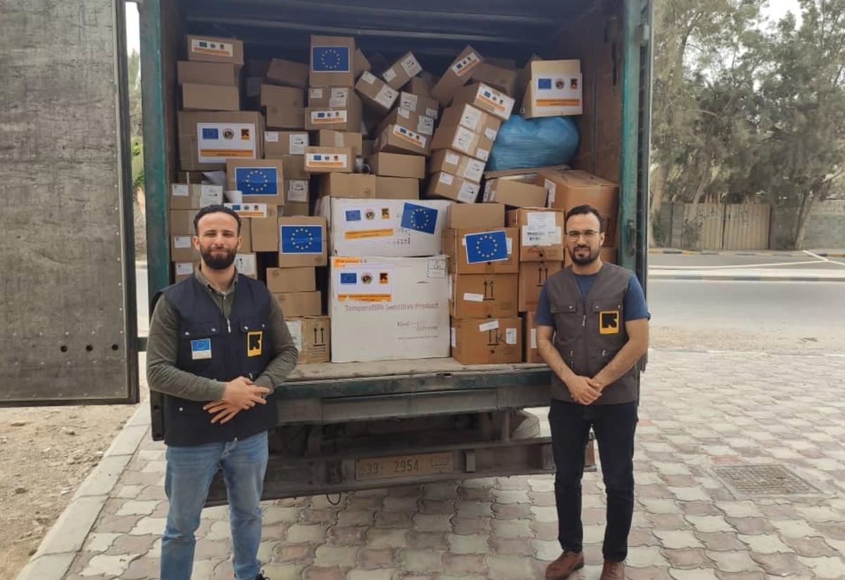 IRC workers deliver supplies to combat COVID-19 in Libya. Two men wearing IRC vests stand in front of a truck full of boxes of supplies to fight COVID-19, in Libya.