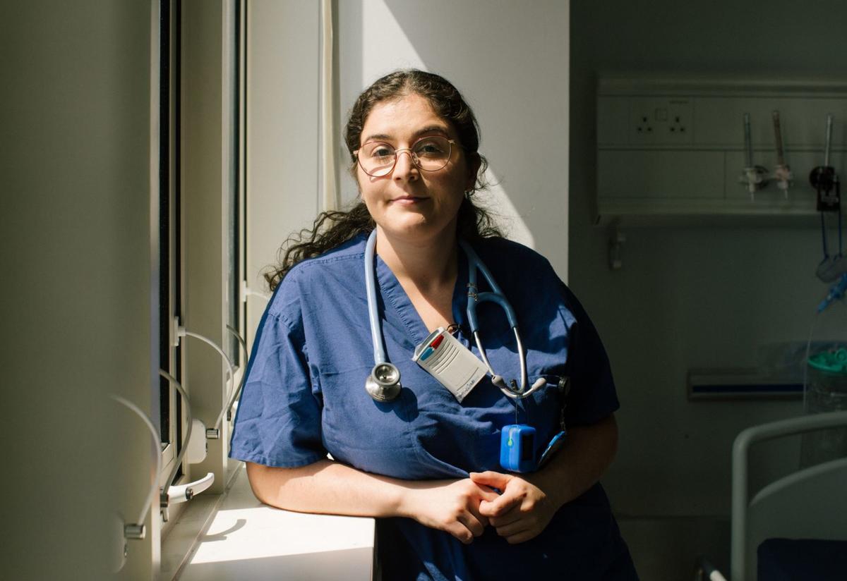 Anxhela Anxhela poses in her scrubs by a window. She is wearing a stethoscope.