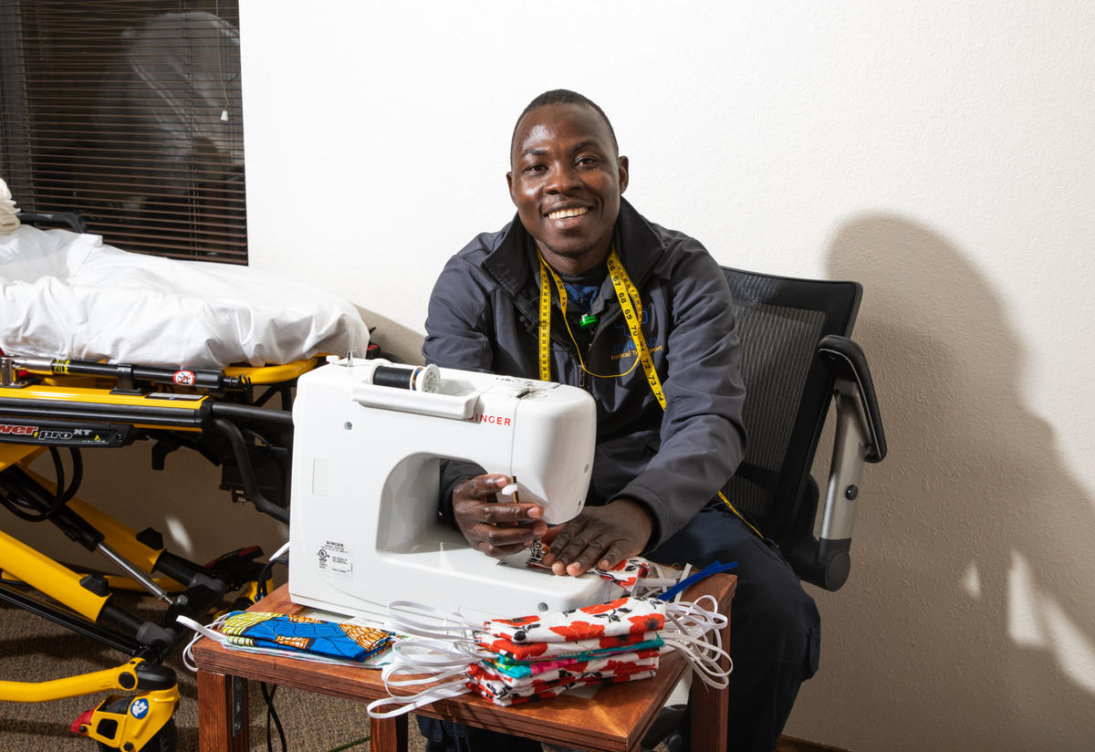 Jonathan Amissa at the desk where he sews masks Jonathan Amissa sits at the desk where he sews masks. There is a white sewing machine and a stack of masks on the desk.