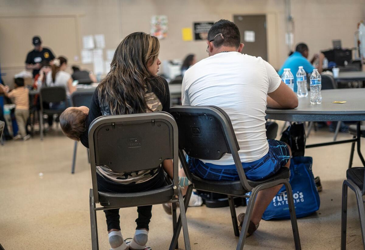 In the IRC's Welcome Center for asylum seekers, a husband and wife sit with their back to the camera as they discuss their journey as asylum seekers. The wife is holding their 2-year-old daughter. 