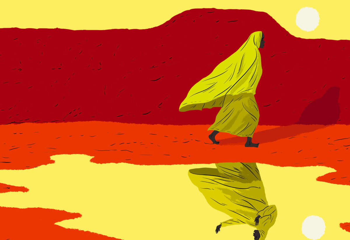 Marie, a woman who journeyed from Cameroon to Niger, walks next to a lake that shows her reflection. She is wearing a yellow head scarf and there is a red mountain behind her. 
