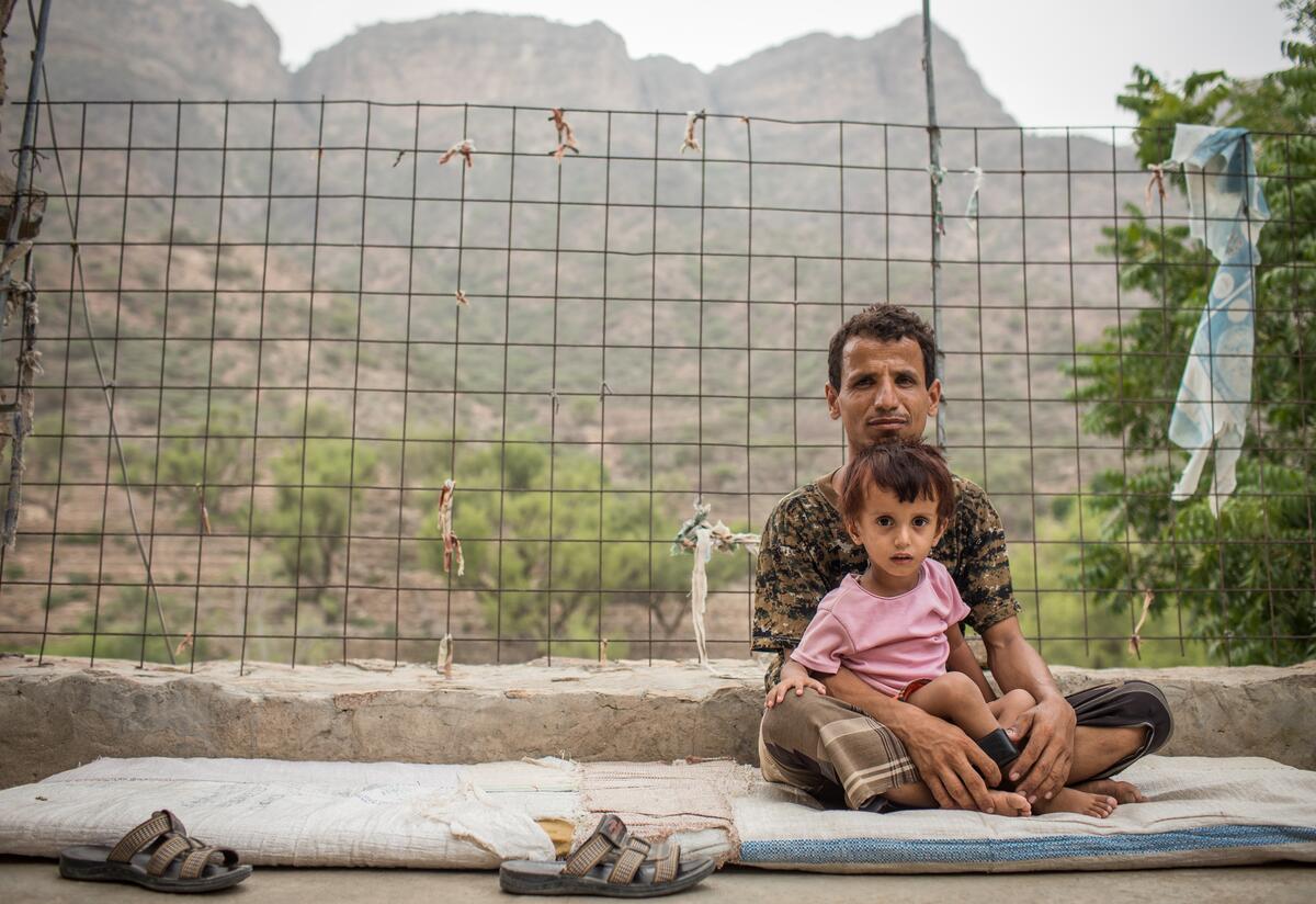 A man sits outside holding his child in his lap in a mountain village in Yemen where an IRC mobile health team provides care to families affected by conflict.