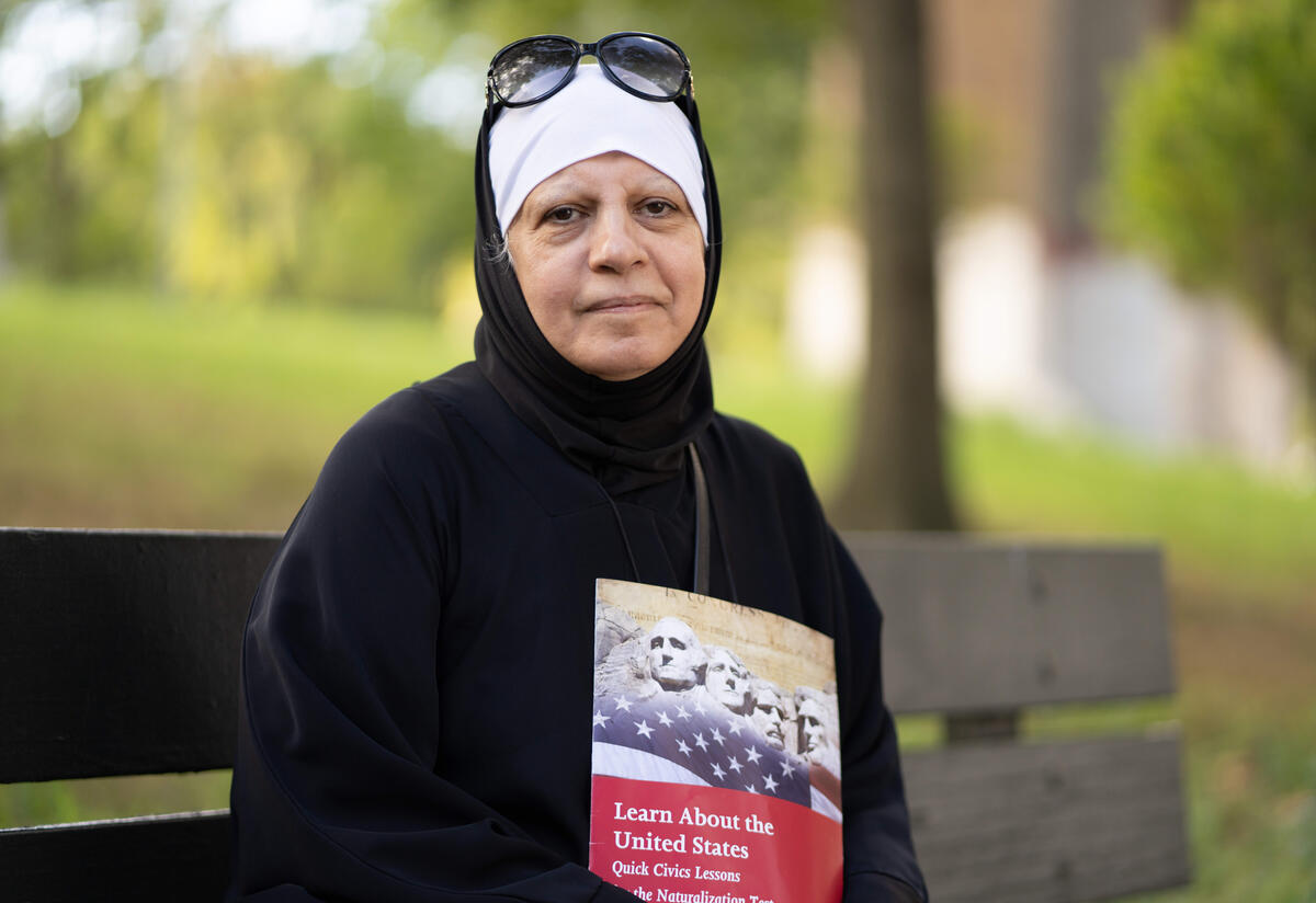 Maha, a refugee from Iraq and new American citizen, sits on a park bench in Queens, NY, holding a book on the U.S. citizenship test. 