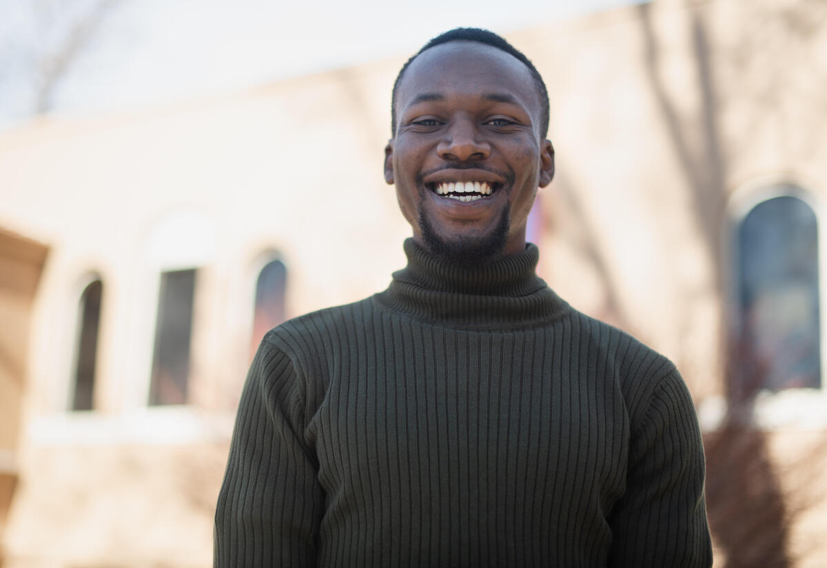 Fredrick Shema, outside and wearing a green sweater, smiles. 