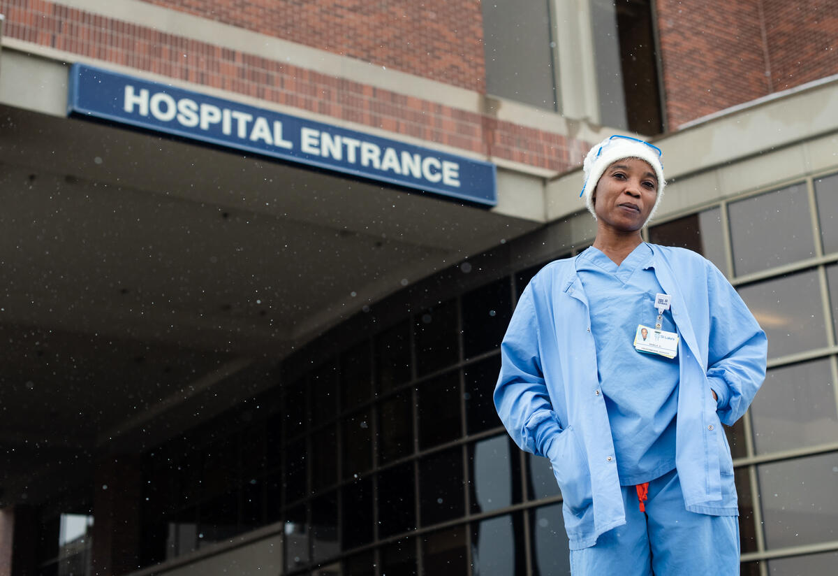 Nabila at hospital Nabila in front of the hospital where she works. She is wearing blue scrubs.
