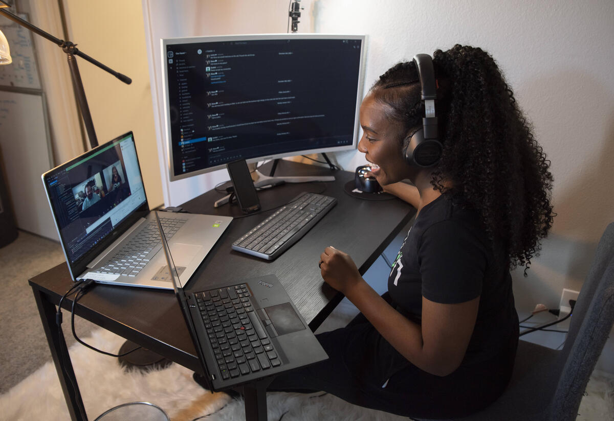 Diana works with her team Diana sits at a desk with two laptops and a monitor. She is wearing headphones and talking to her employees at Clyn.
