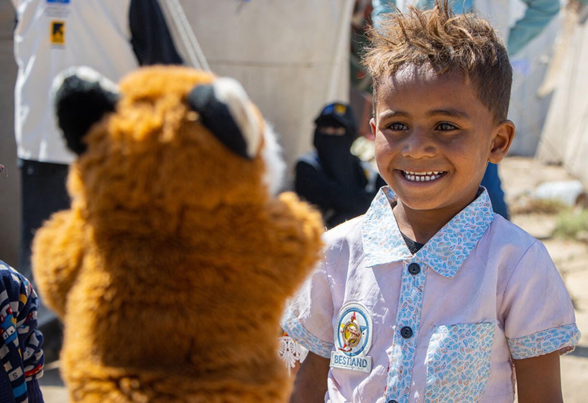 Outside in Al-Manshar camp, five-year-old Yasser laughs while looking at a fox puppet 