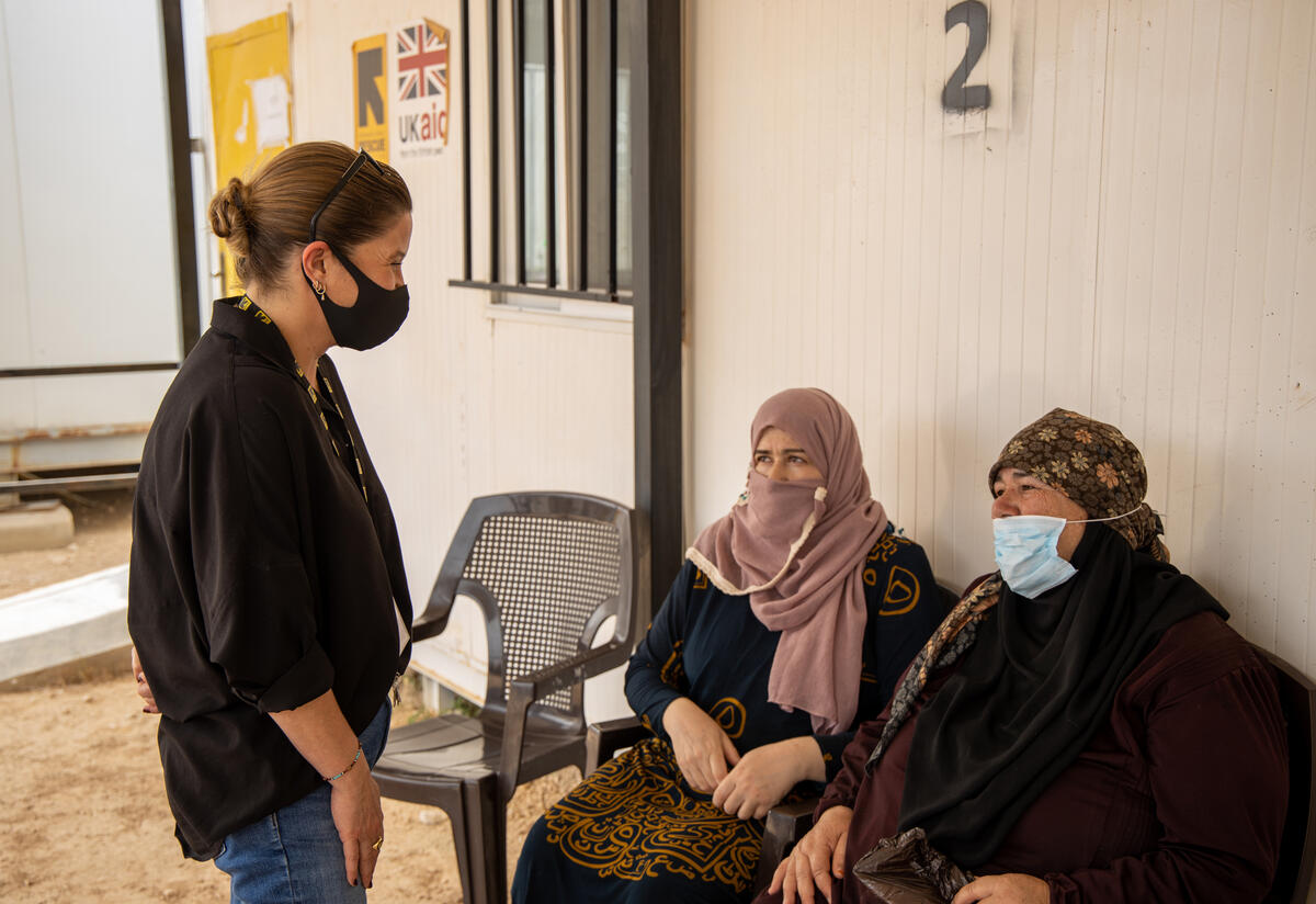 Sarra Ghazzi, IRC country director in Jordan stands speaking with two seated Syrian women waiting to get COVID-19 vaccinations at an IRC clinic.