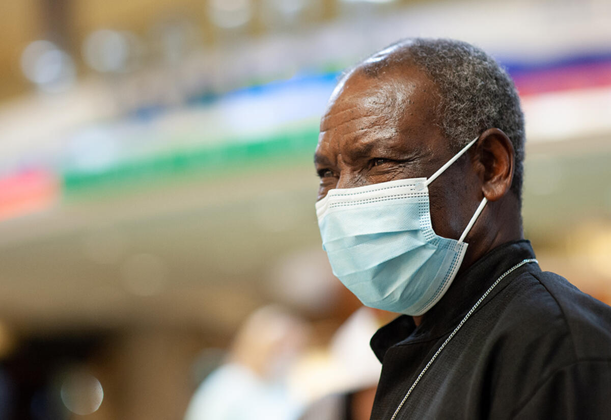 Patrice Maneno waiting at the airport for his daughter Mauwa A close up of Patrice at the airport waiting for his daughter. He is wearing a mask.